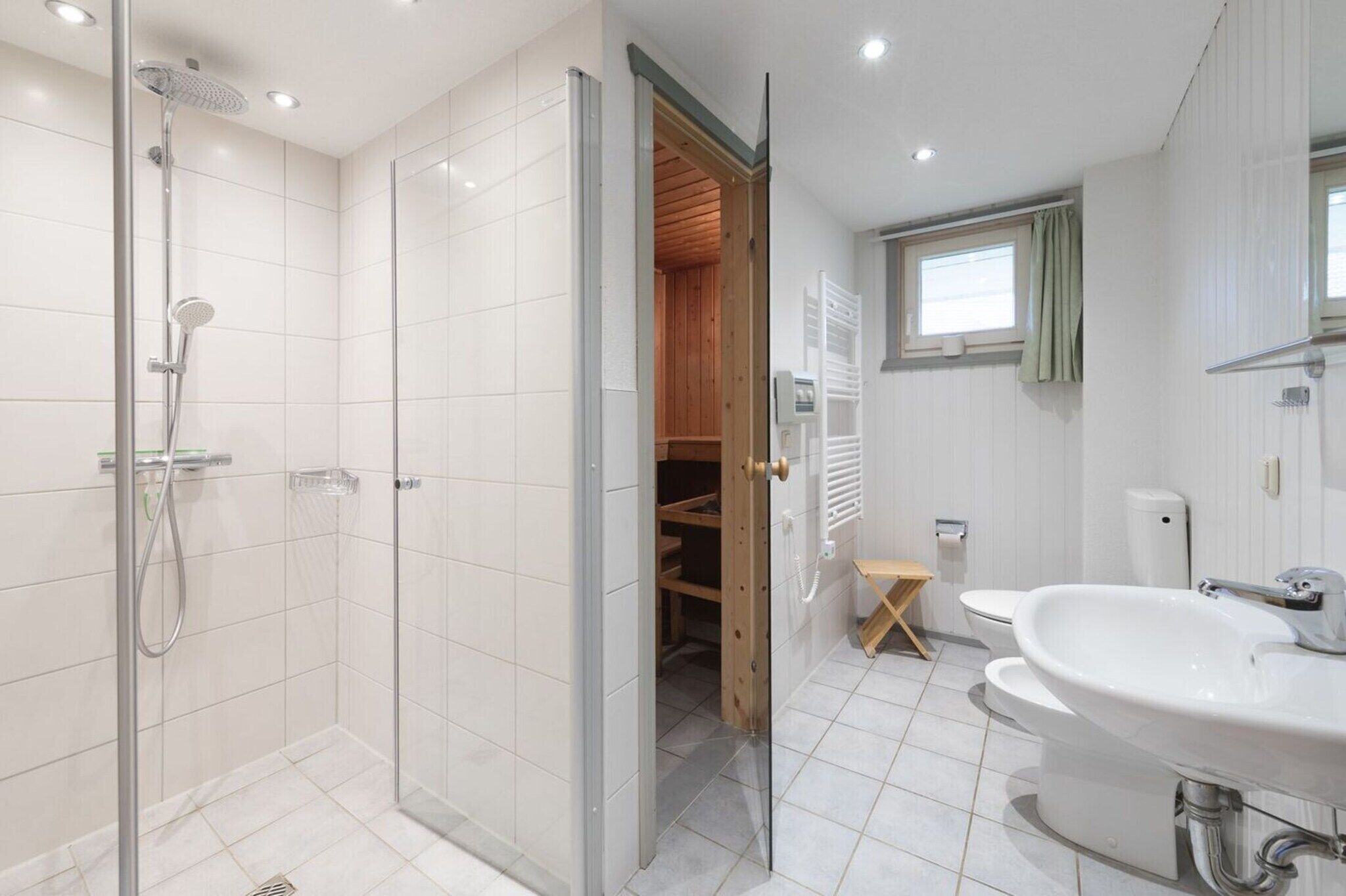Een moderne badkamer met een glazen douchecabine, een inloopkast met houten deuren en een witte wastafel.