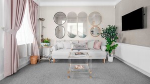 A living room with a white sofa, a glass coffee table, and a large mirror collection on the wall.