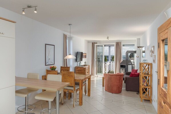 A modern living room with a dining area, a fireplace, and a view through a glass door.