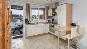 A compact kitchen with a wooden table, two bar stools, and a view of the outdoor deck. - Appartement im Ferienpark in Rechlin (Rechlin)