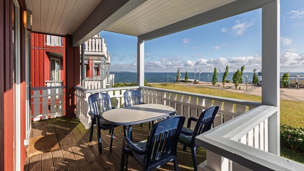 A covered outdoor area with a table and chairs, overlooking a body of water and a distant building.