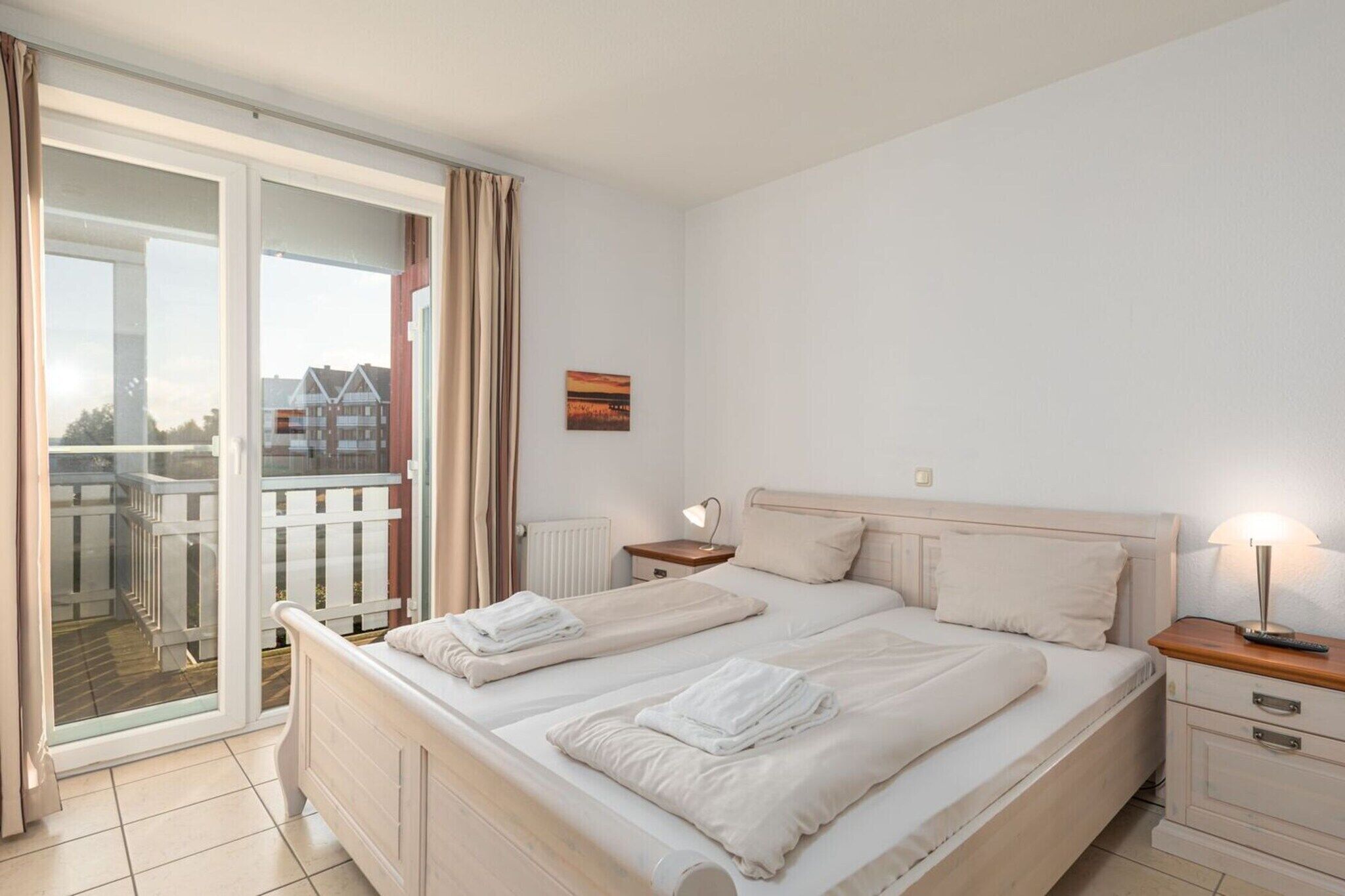 Een hotelkamer met twee bedden, een balkon, een schilderij en een lamp.