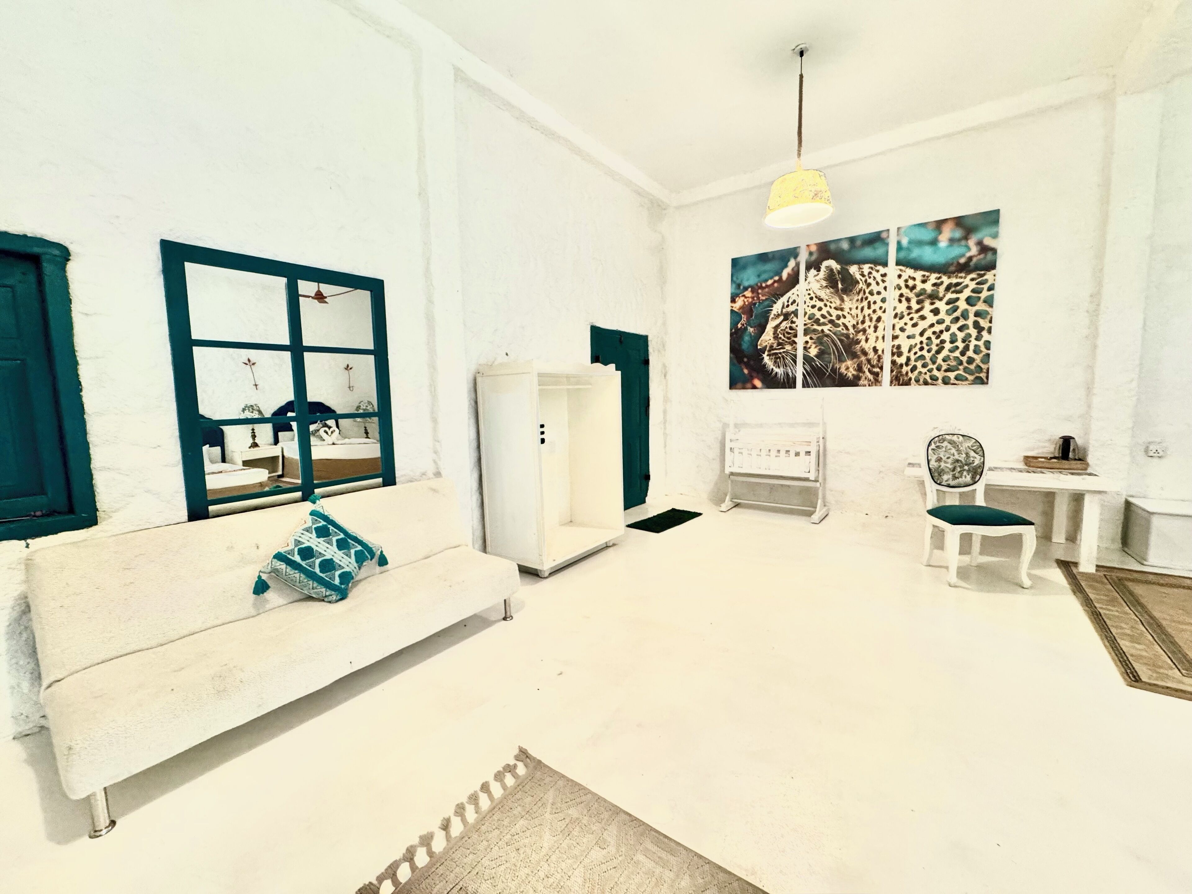 A room with a white sofa, a small table, a chair, a radiator, and a painting of a leopard.