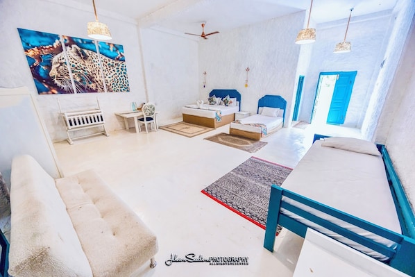 A modern bedroom with a large leopard print artwork, a bed with a blue headboard, a desk, and a chair. - Epic Wild Wilpattu (Nochchiyagama)
