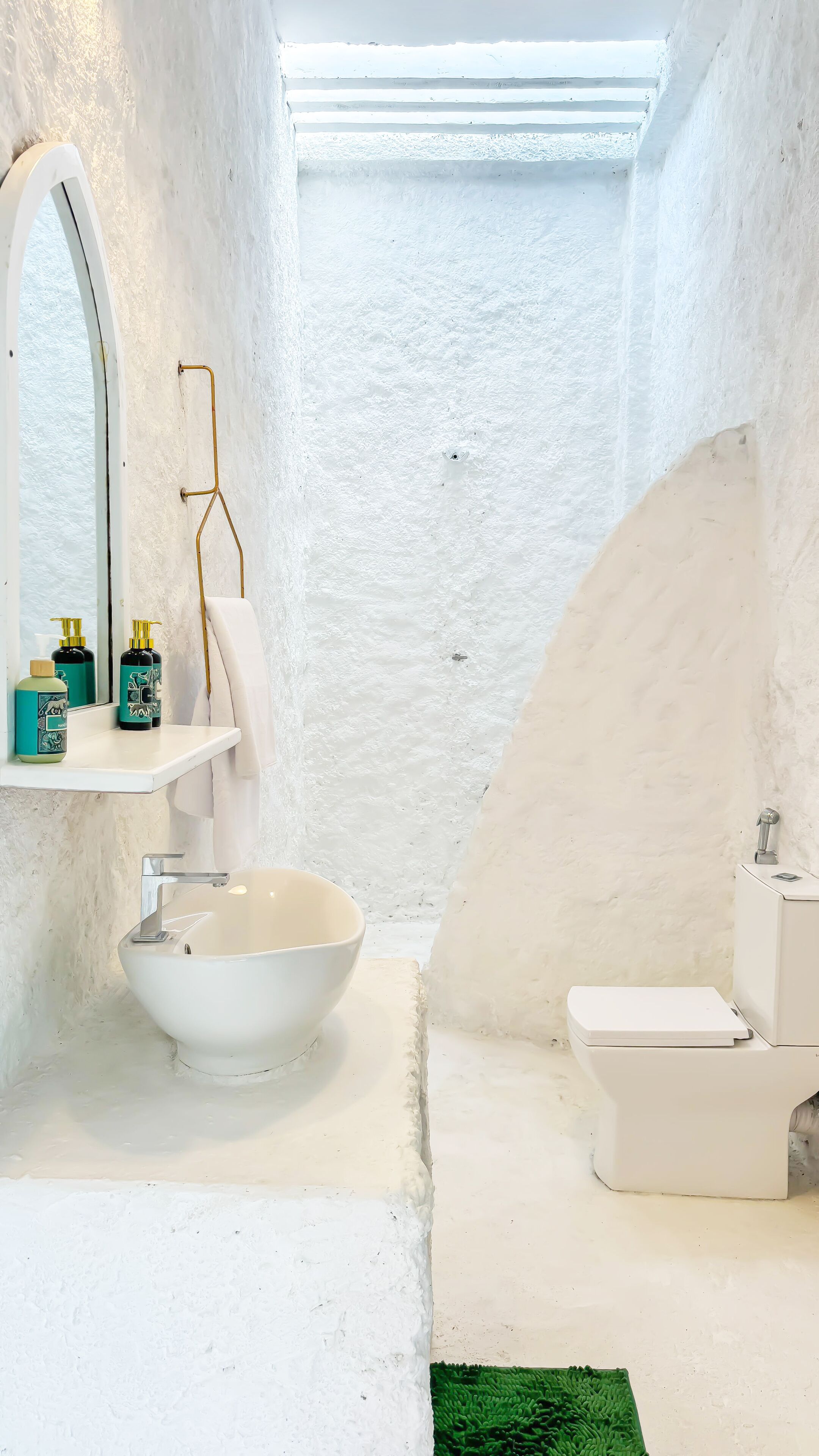 A bathroom with a white sink, a mirror, and a toilet. There is a towel hanging on the wall.