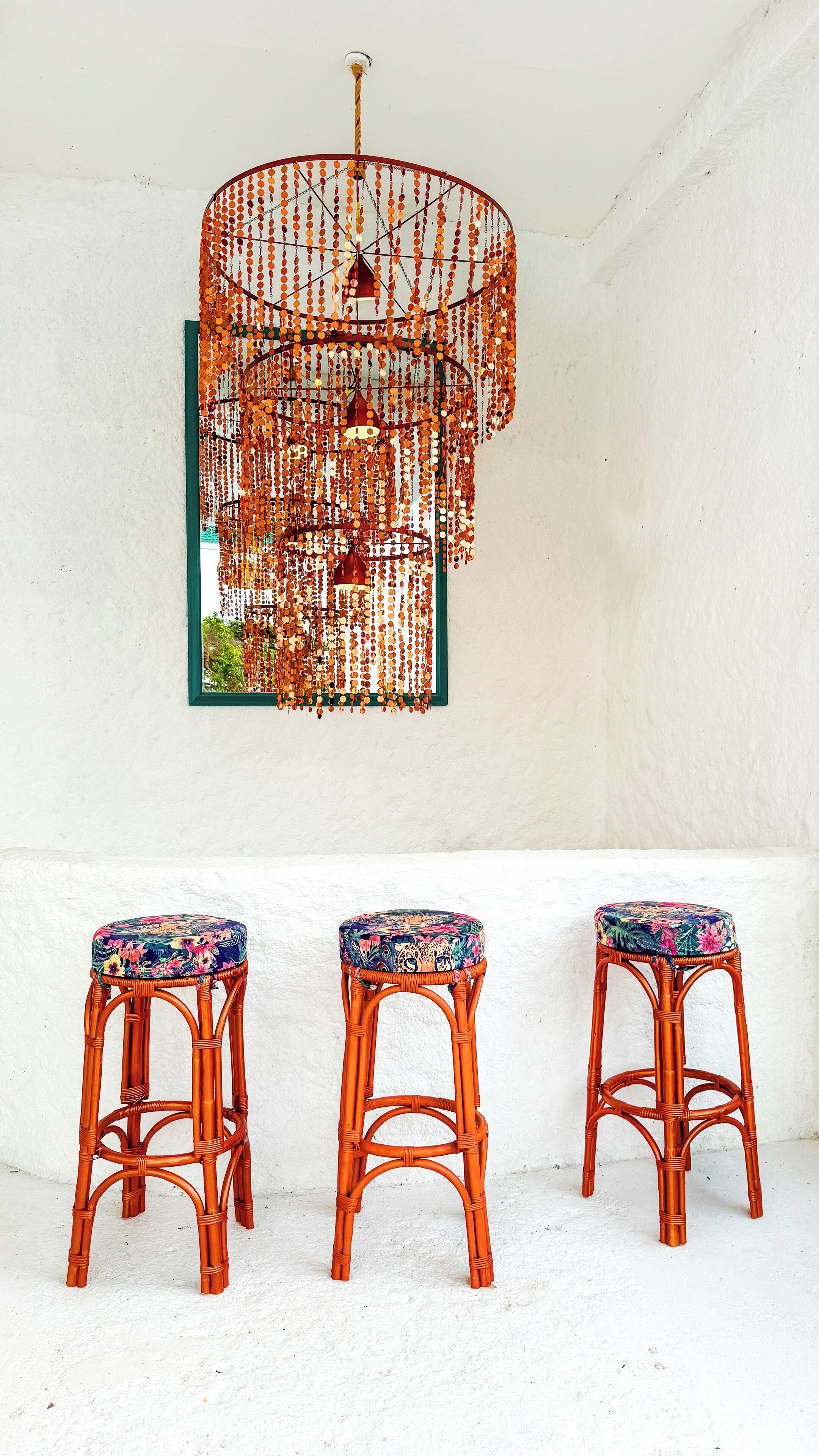 A room with three wicker stools with colorful cushions and a decorative hanging light fixture.