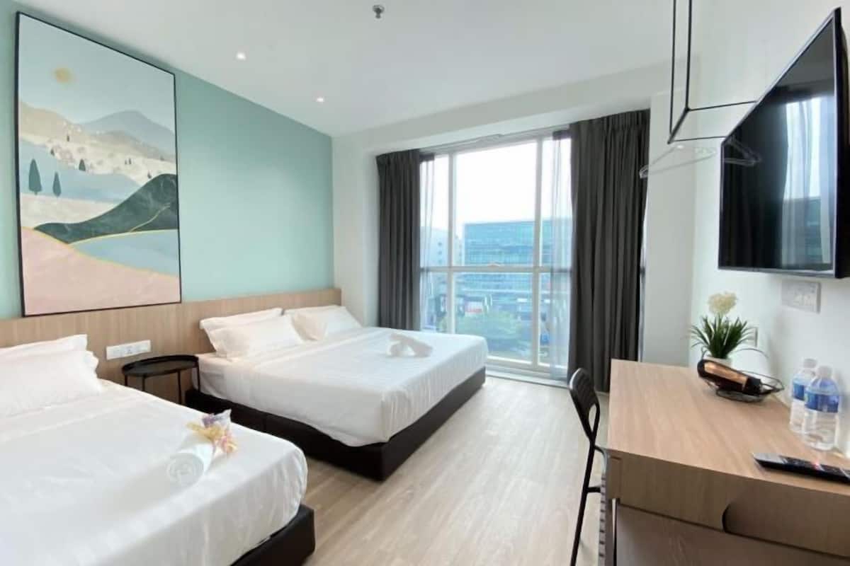 Habitación de hotel con dos camas, un escritorio, un televisor y un ventanal con cortinas.