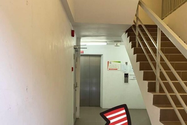 Un pasillo con una escalera a la derecha, una puerta al final y un detector de incendios en la pared.