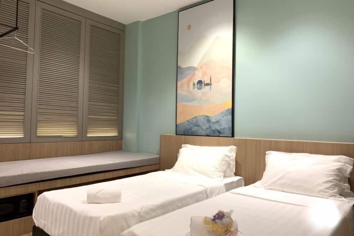 Habitación de hotel con dos camas, un banco, un ventanal con persianas y un cuadro en la pared.