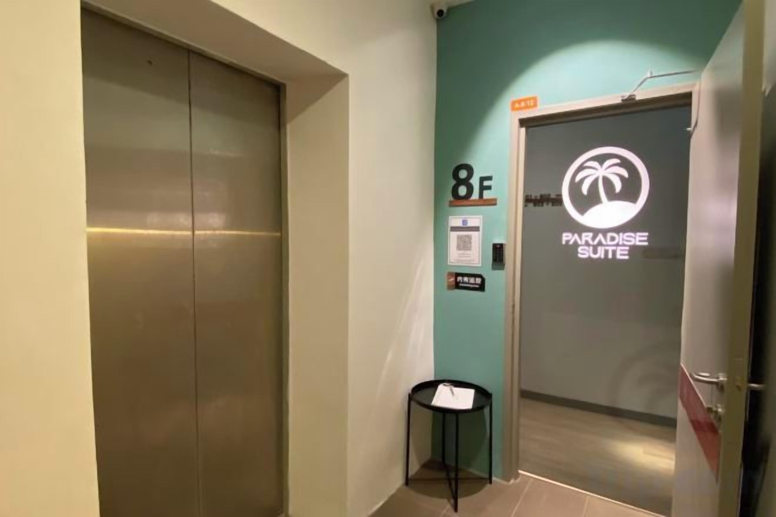 A hallway with an elevator, a door labeled '8F Paradise Suite,' and a small table with a chair.