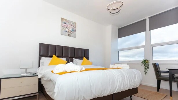 A modern hotel room with a large bed, a bedside table, a chair, and a window with a view of the sky. - Flat 308 One bedroom Apartment (Smethwick)