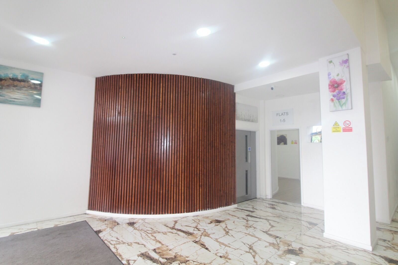 Un hall d’entrée doté d’un comptoir de réception en bois aux lignes courbes, d’un sol en marbre et d’un tableau accroché au mur.