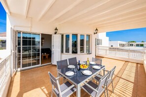 Un espacio de comedor al aire libre techado con una mesa preparada para cuatro personas, puertas de vidrio correderas y vistas a la ciudad.