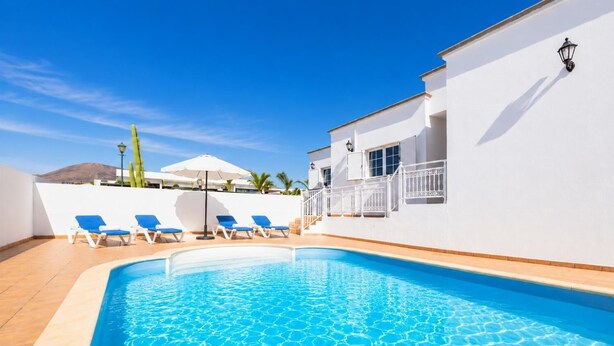 Ein Swimmingpool mit blauem Wasser, umgeben von weißen Wänden und einigen blauen Liegestühlen.