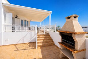 A covered outdoor area with a barbecue grill, a staircase, and a white railing.