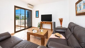 Ein Wohnzimmer mit einer Couch, einem Couchtisch, einem Fernseher und einer Glastür, die auf einen Balkon führt.