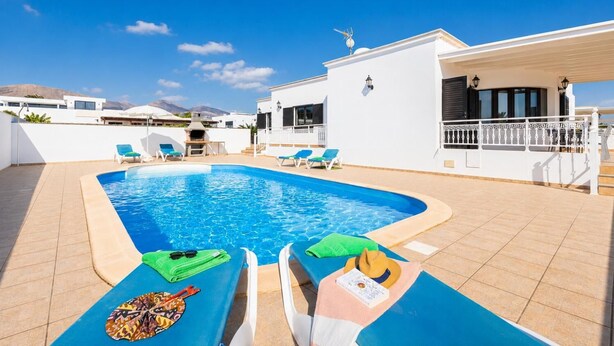 Ein Schwimmbad mit Liegestühlen, einem Grill und einem weißen Gebäude mit Balkon.