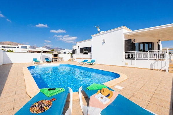 Ein Schwimmbad mit Liegestühlen, einem Grill und einem weißen Gebäude mit Balkon.
