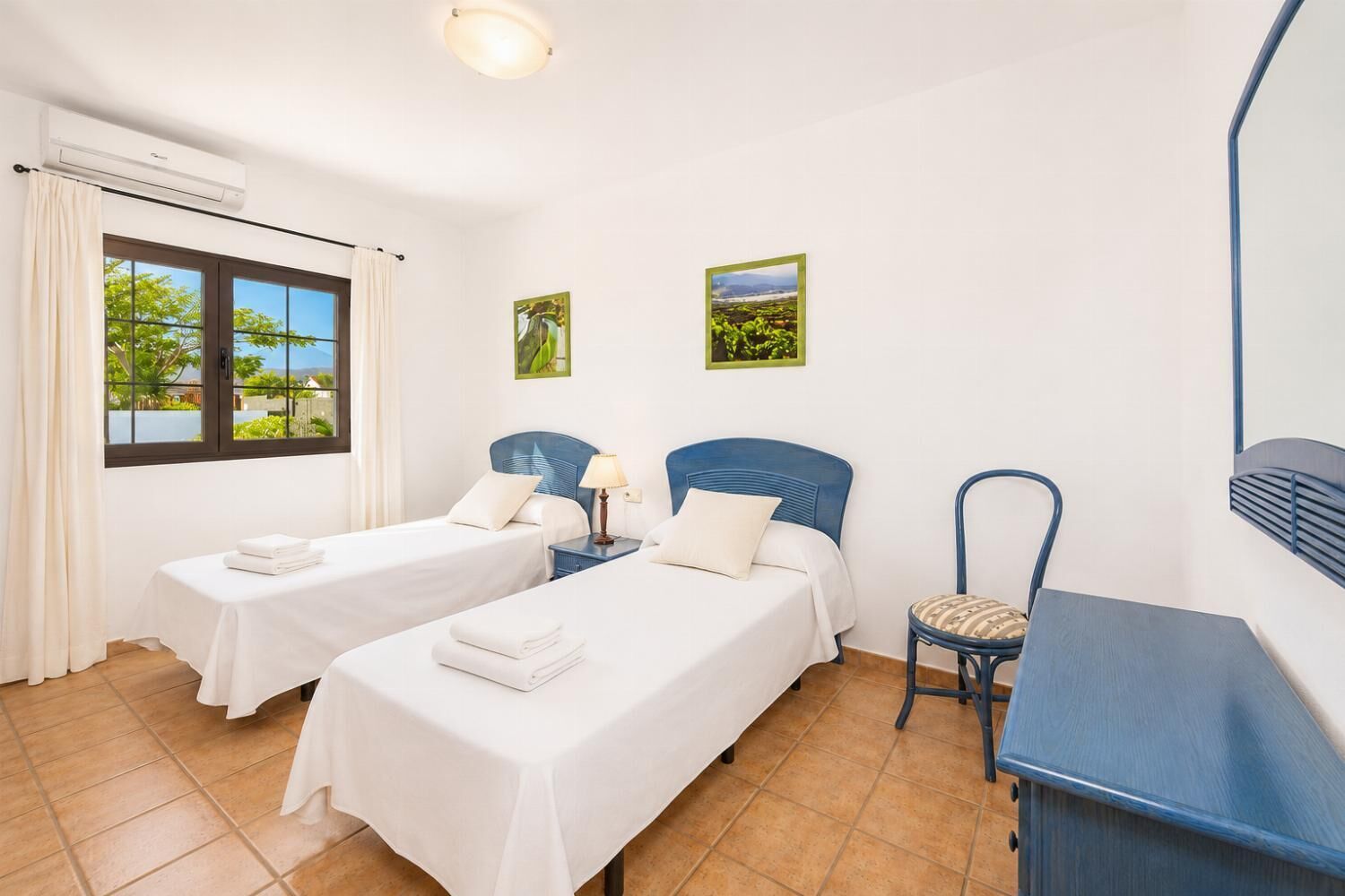 Une chambre d’hôtel avec deux lits, un bureau, une chaise et une fenêtre donnant sur un paysage verdoyant.