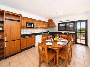 Une cuisine avec des meubles en bois, une table à manger dressée pour quatre personnes et une vue sur l’extérieur, accessible par une porte-fenêtre coulissante.