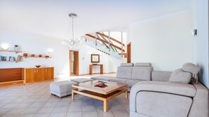 Una sala de estar moderna con un sofá, un reposapiés y una mesa de centro. Se ve una escalera que sube a otro nivel.