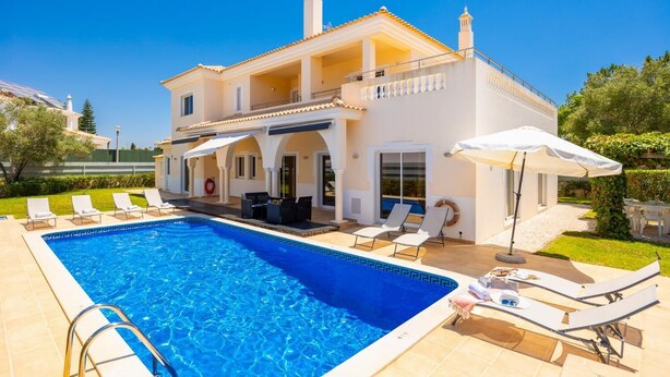 Una casa de dos pisos con piscina, mobiliario exterior y jardín.