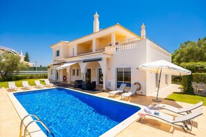 Una casa de dos pisos con piscina, mobiliario exterior y jardín.