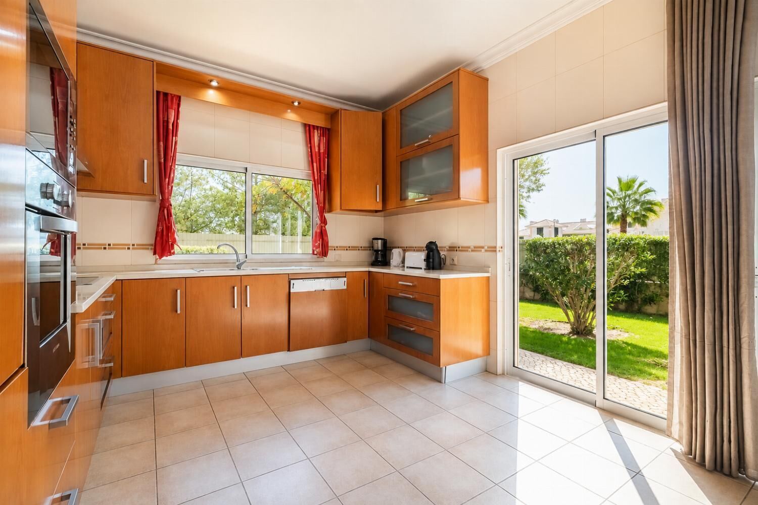 Une cuisine moderne avec des meubles en bois, un four encastré et une grande fenêtre donnant sur un jardin.