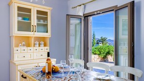 Un comedor con una mesa dispuesta para cuatro, un armario de madera con puertas de cristal y vistas al exterior a través de una puerta corrediza de vidrio.