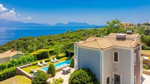 Una villa con piscina, vista al mar y un paisaje montañoso al fondo.