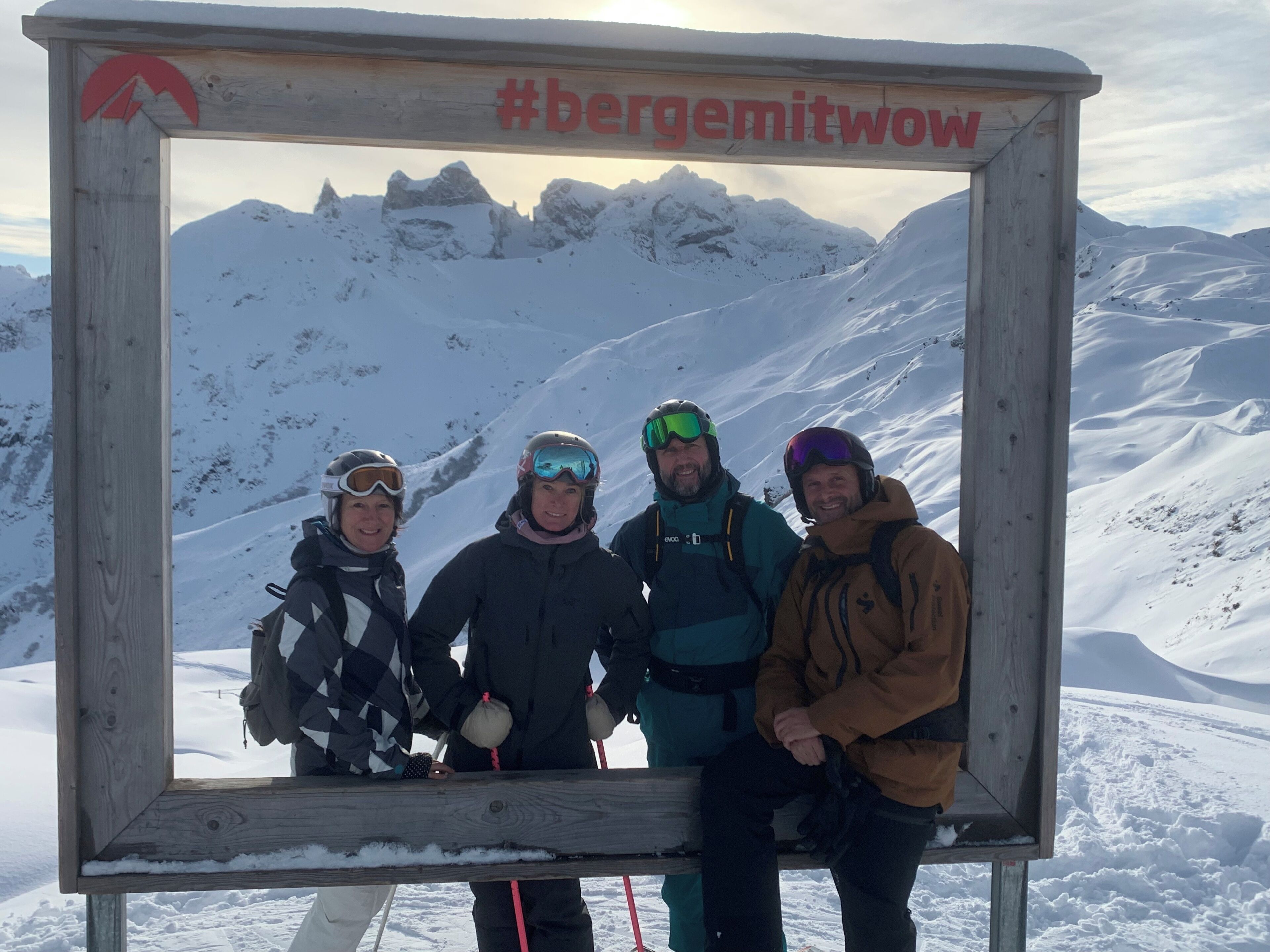 A group of people posing in front of a wooden sign with a mountain view in the background.