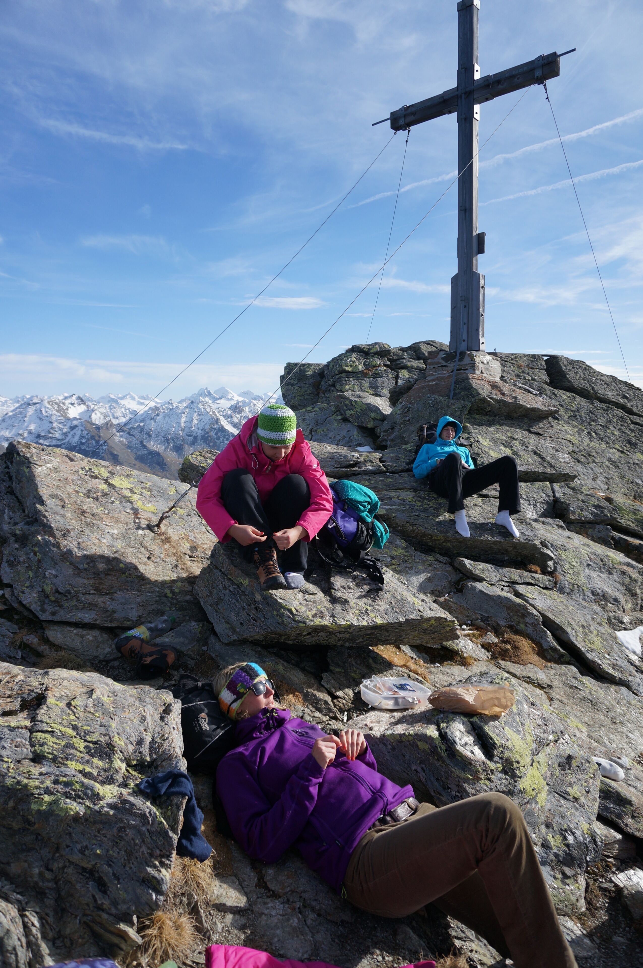 Un grupo de personas descansando en la cima de una montaña rocosa, con una estructura en forma de cruz al fondo.