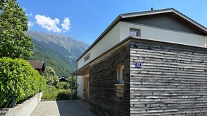 A modern building with a wooden facade, a paved pathway, and a mountain view in the background.