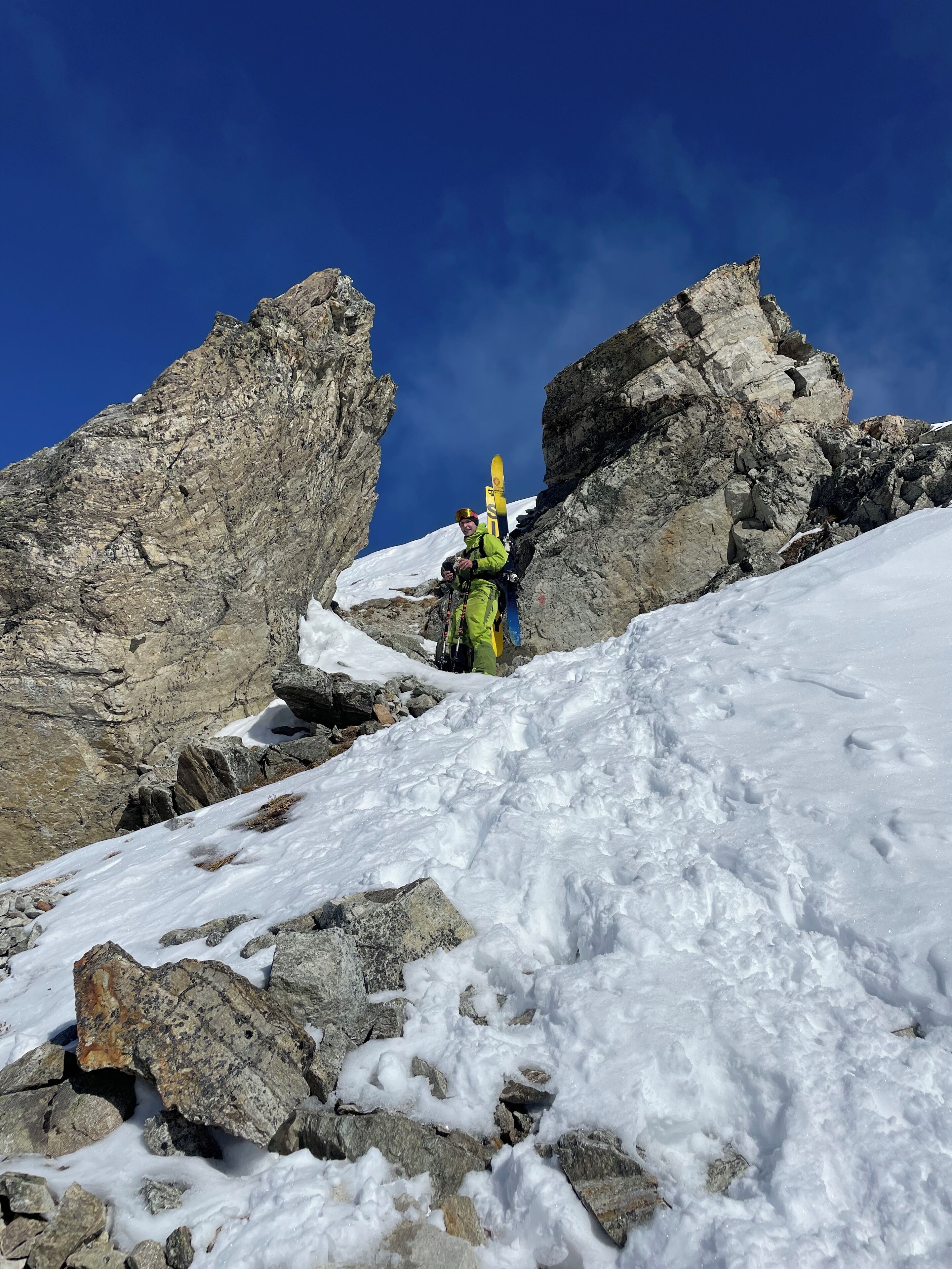 A snowy mountain landscape with rocky terrain and a clear blue sky.