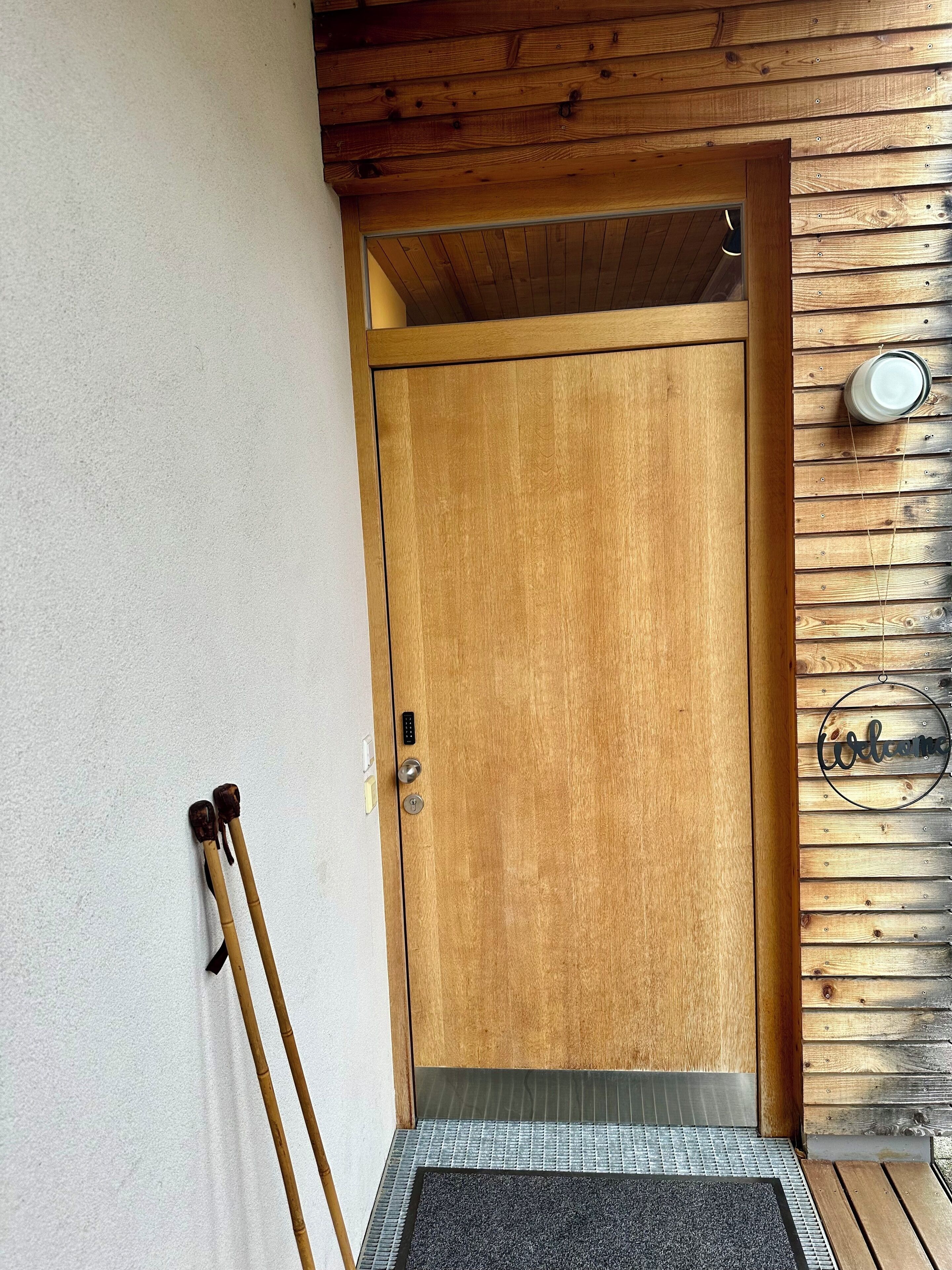 A wooden door with a metal handle, a doormat, and a welcome sign on a wooden wall.