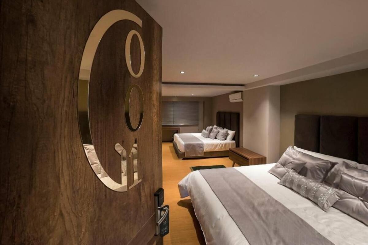 A modern bedroom with two beds, a large mirror, and a wooden accent wall.
