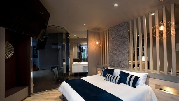 A modern bedroom with a large bed, a glass partition, and a unique light fixture. - ALBURA HOTEL (Pereira)