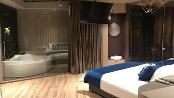 Quarto de hotel moderno com uma cama grande, hidromassagem em vidro e uma televisão de tela plana.