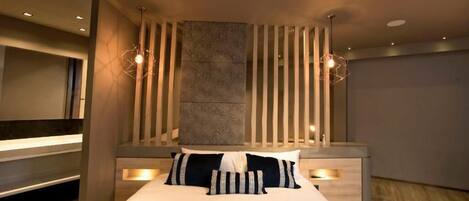 A modern bedroom with a large bed, wooden slats, and a stone accent wall.