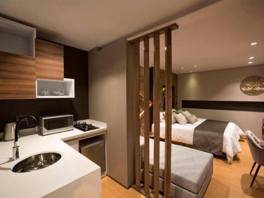 A modern hotel room with a kitchenette, a bed, a seating area, and a decorative wall piece.