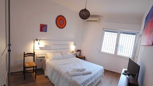 Ein Schlafzimmer mit Bett, Stuhl, Schreibtisch und Computer, sowie einem Fenster.