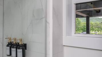 A modern bathroom with a marble wall, a glass shower enclosure, and a window with a view of greenery.