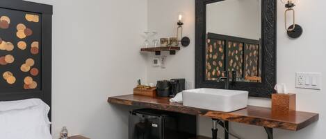 Habitación de hotel con una cama, un refrigerador pequeño, un lavamanos y un espejo con marco decorativo.