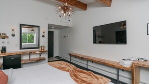 Een moderne slaapkamer met een bed, een houten bankje, een spiegel, een televisie en een plafondlamp.