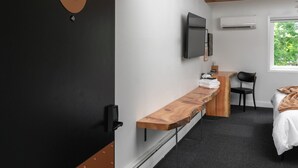 A modern hotel room with a wooden bench, a bed, a desk, a chair, and a TV mounted on the wall. - Lincoln Boutique Motel- Upper Deluxe King #11 (Ellicottville)