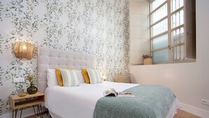 A bedroom with a large bed, a bedside table with a lamp, and a window with a view. - Charming apartment in Malaga center. San Agustin VIII (Malaga)