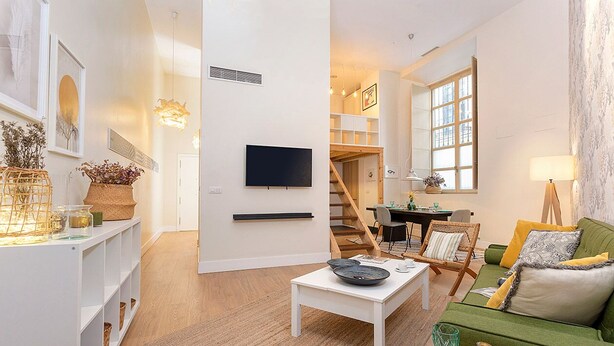 A modern living room with a flat-screen TV, a green sofa, and a dining area with a staircase. - Charming apartment in Malaga center. San Agustin VIII (Malaga)