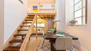 A modern kitchen with wooden cabinets, a dining area with a table set for two, and a staircase leading to an upper level. - Charming apartment in Malaga center. San Agustin VIII (Malaga)