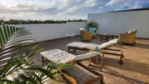 Una terraza en la azotea con sillones de descanso, una mesa y una planta en maceta.