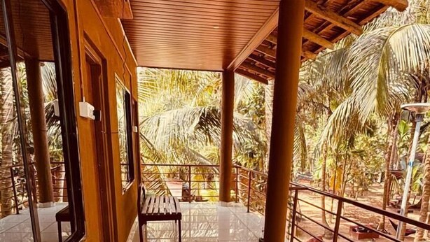 A covered outdoor seating area with a bench, wooden columns, and a view of palm trees. - Experience Gokarna - A Slow-Paced Backpackers Community (Gokarna)